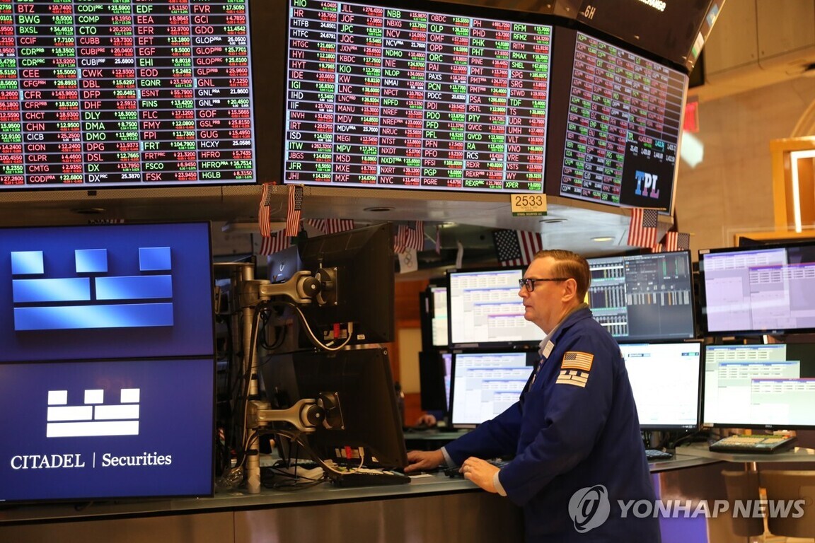 주식 시장 거래소 내부에서 여러 대의 모니터와 전광판을 바라보며 일하는 남성 트레이더의 모습