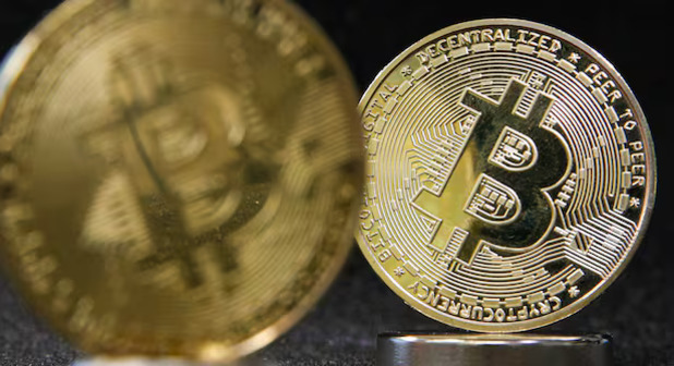 비트코인 로고가 새겨진 두 개의 금색 동전이 어두운 배경 위에 놓여 있다.